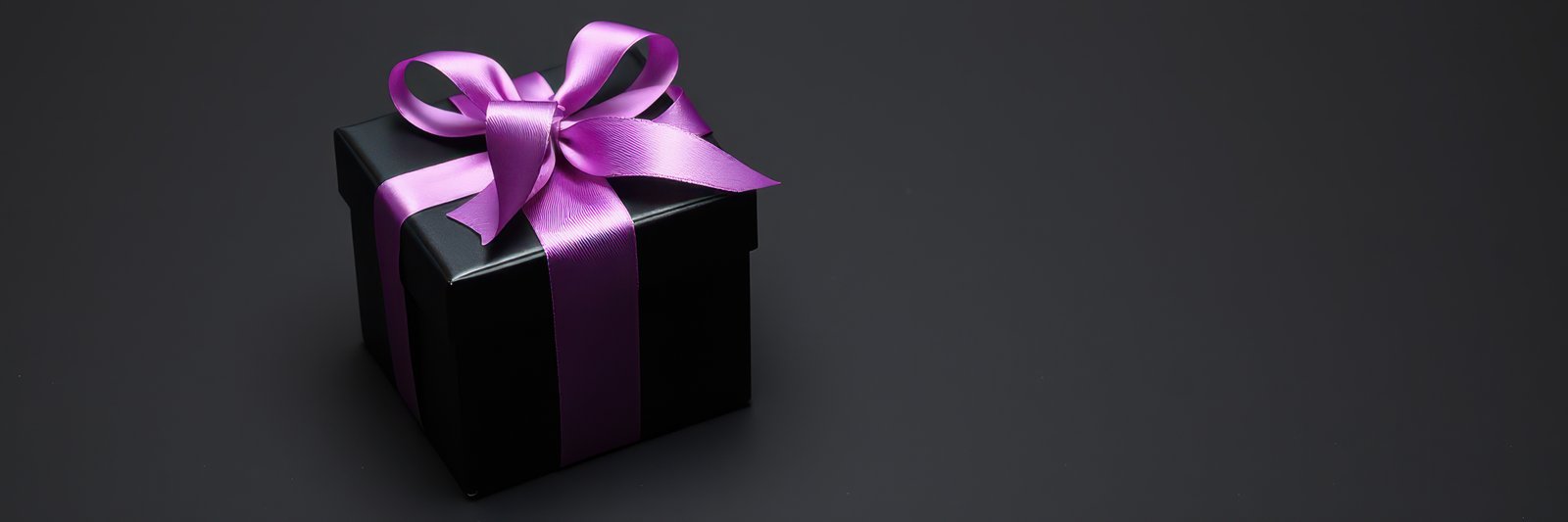 Elegant black gift box with purple ribbon on dark background ready for giving